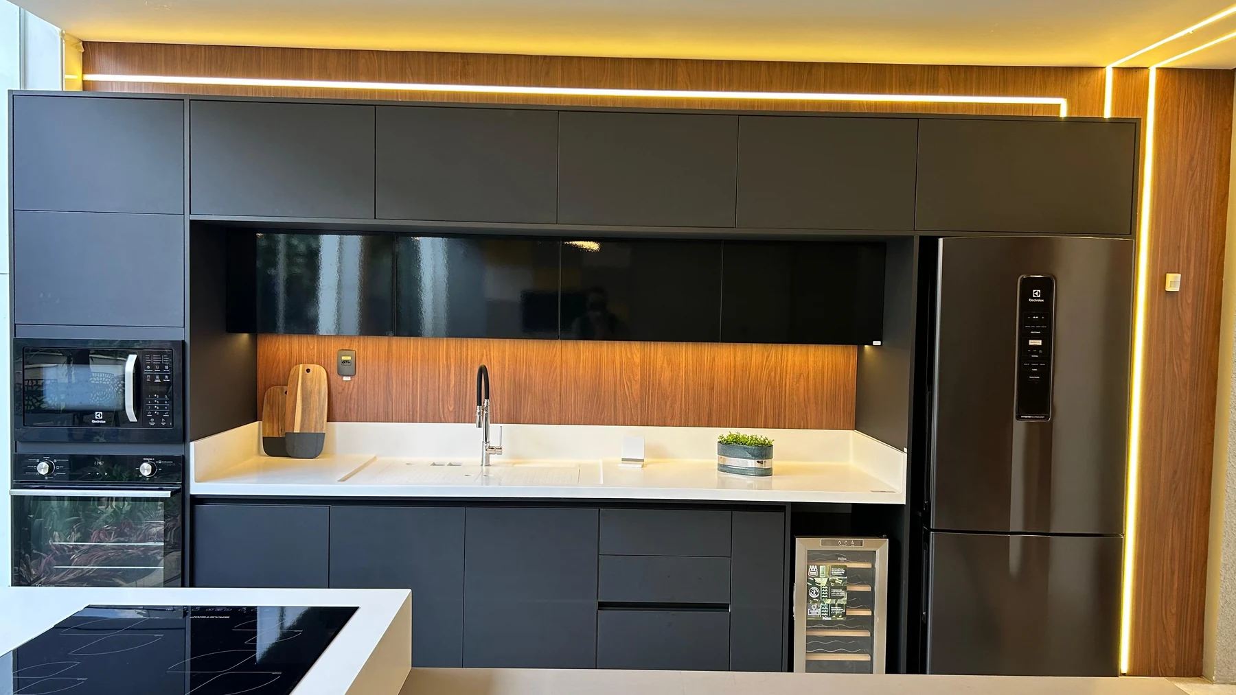 Cozinha real com marcenaria escura, bancada clara e iluminação linear